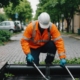 Professional cleaning a commercial storm drain with equipment, urban infrastructure and greenery in the background.